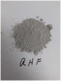 A small pile of gray powder with some larger pellets scattered on a surface with "qhf" written underneath it.