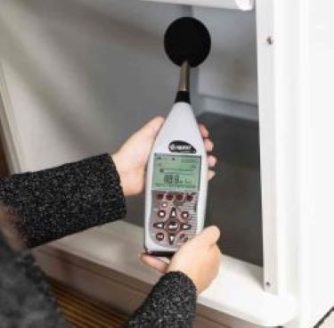 A person holding a sound level meter inside an open ventilation shaft with the meter's display showing a reading of 48.9 decibels.
