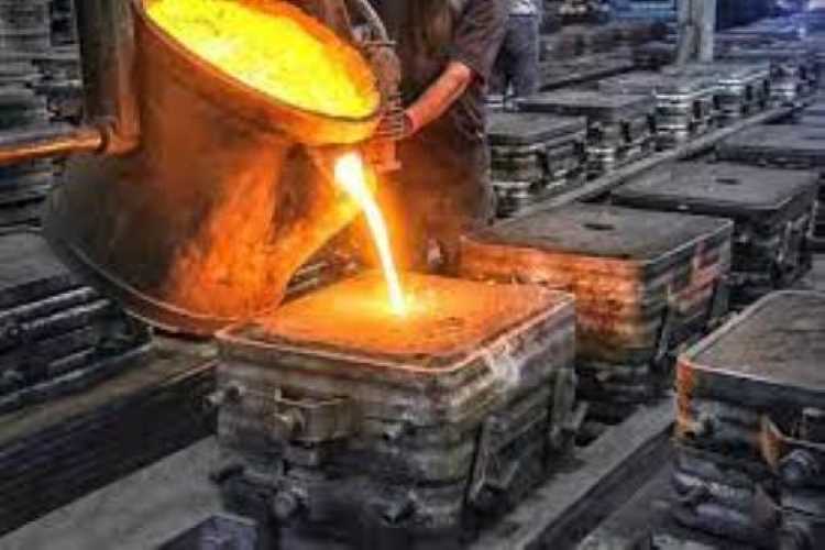 A worker pours molten metal into molds in an industrial foundry setting.