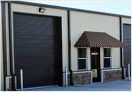 Exterior view of RW Specialty Imports Chemical Warehouse featuring a large closed roll-up garage door and an adjacent entrance.