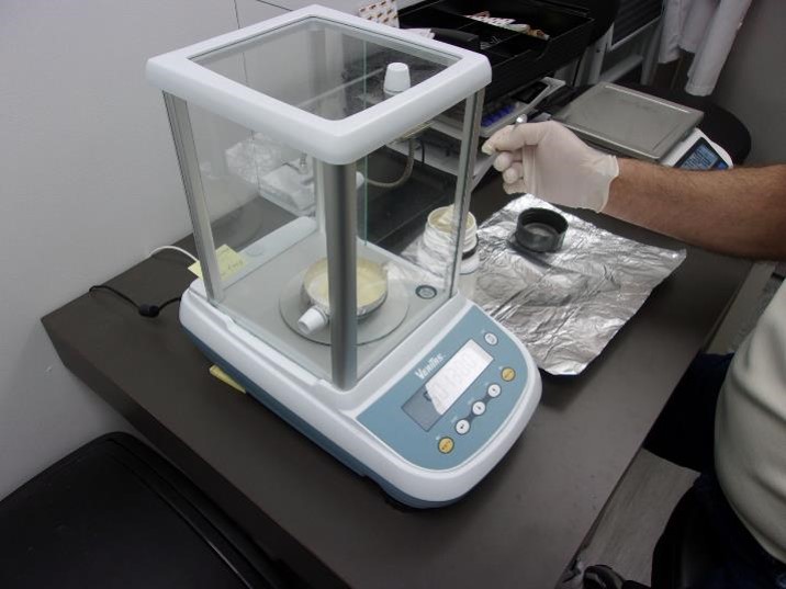 A researcher uses a digital scale inside a glass enclosure to measure a powdery substance in a laboratory setting, part of the meticulous process involved in Microbiology Testing Services.